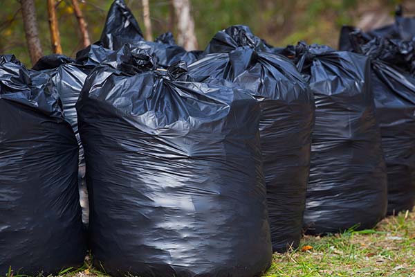 Black, complete and tied garbage bags standing together on the street, outdoors. removal, sorting and recycling rubbish.